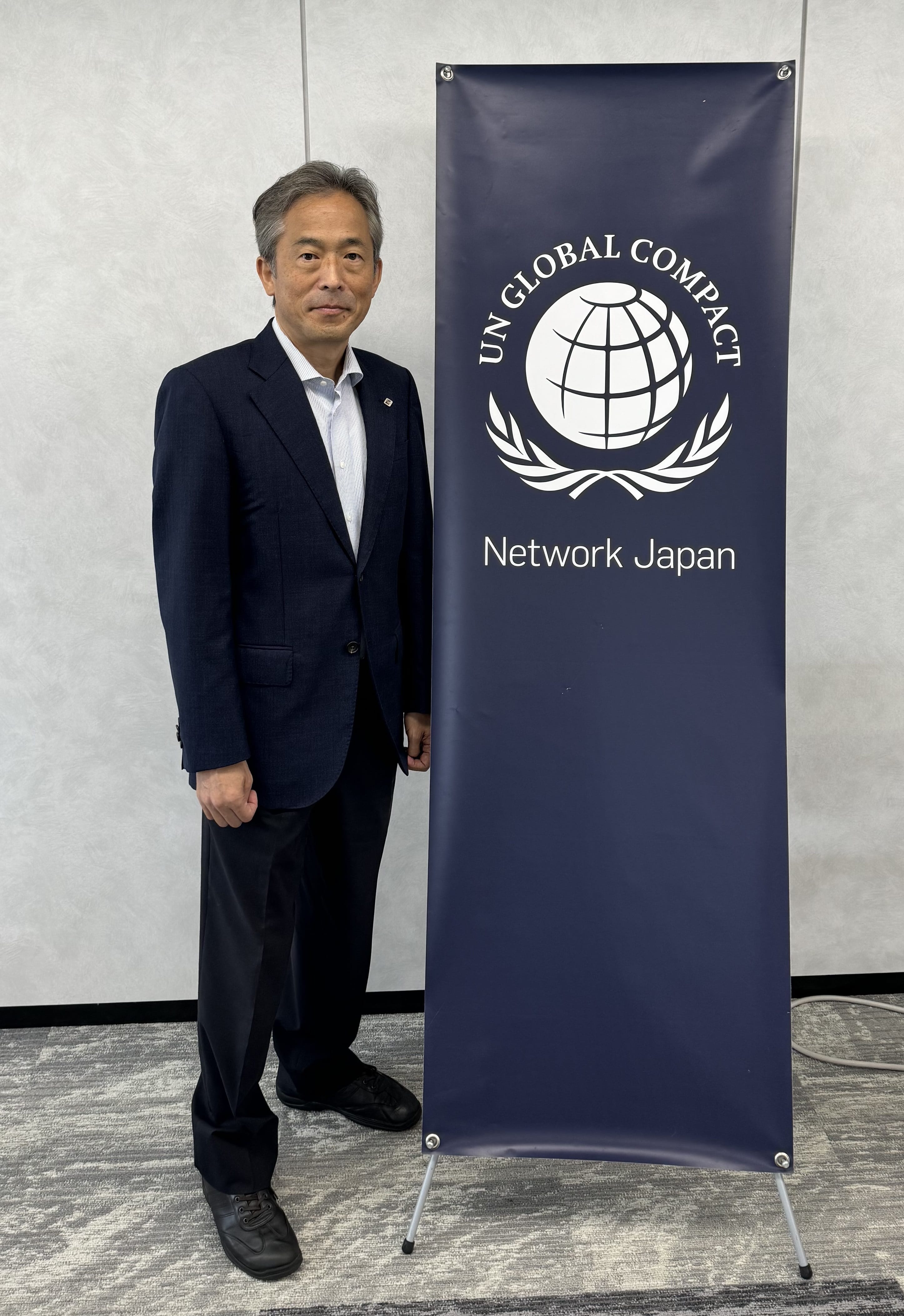 佐藤 博之理事とUN Global Compactロゴの写真